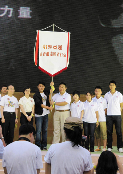 黎明及香港志愿者协会副主席林亨利先生从亚组委志愿者部宣传策划办公室副主任吕娜(右七)手中接过广州亚运会志愿者旗帜后，高高举起。右八为广播处长黄华麒先生。